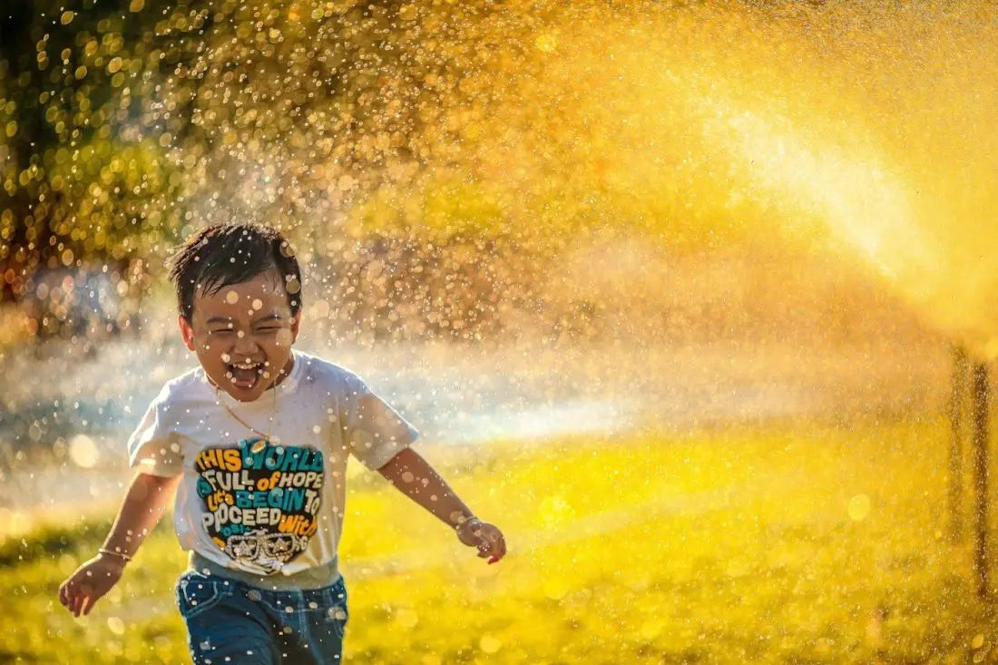 Joyful child laughing and running through a sprinkler